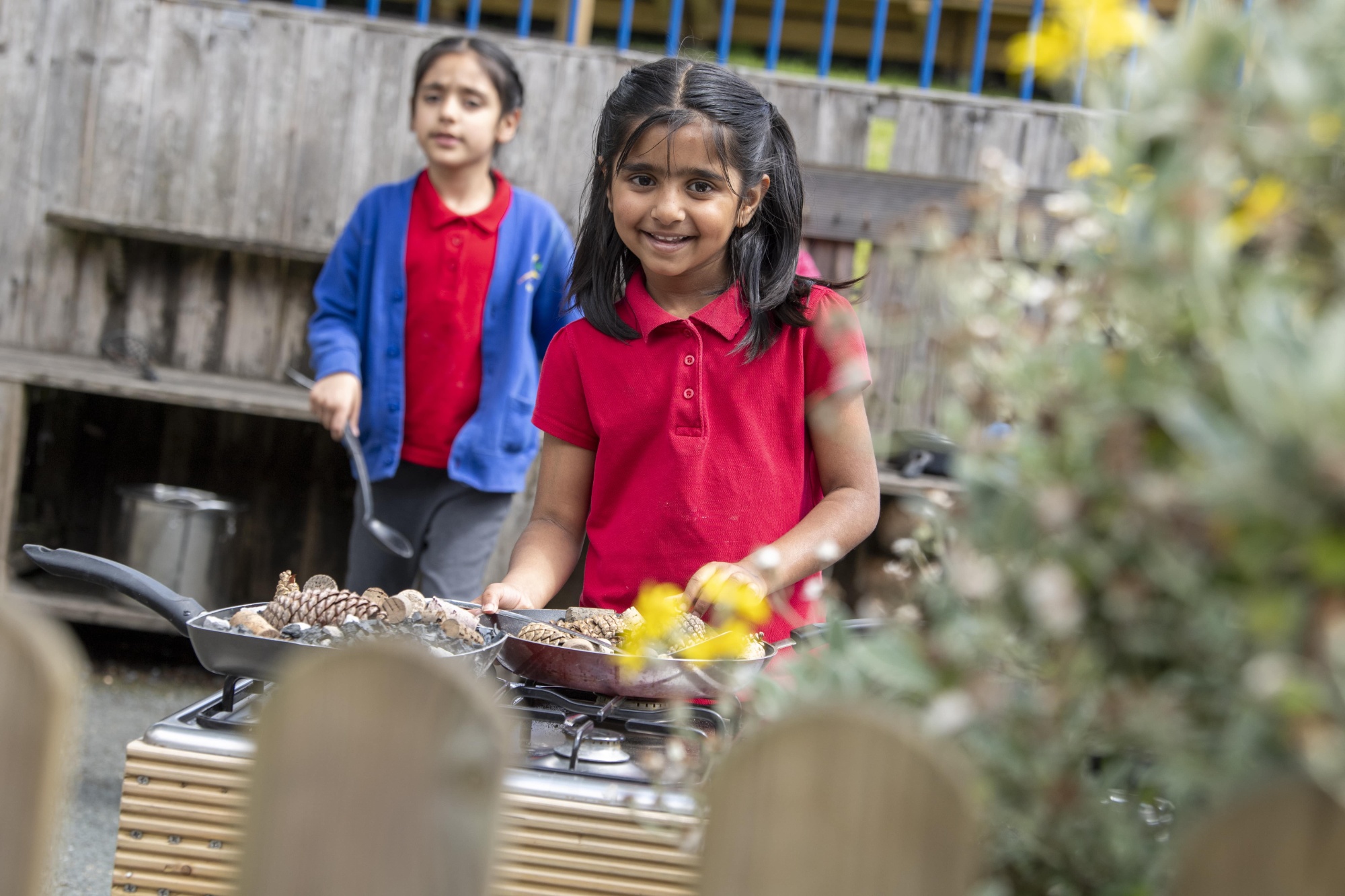 Two children playing with pine cones in a mud kitchen